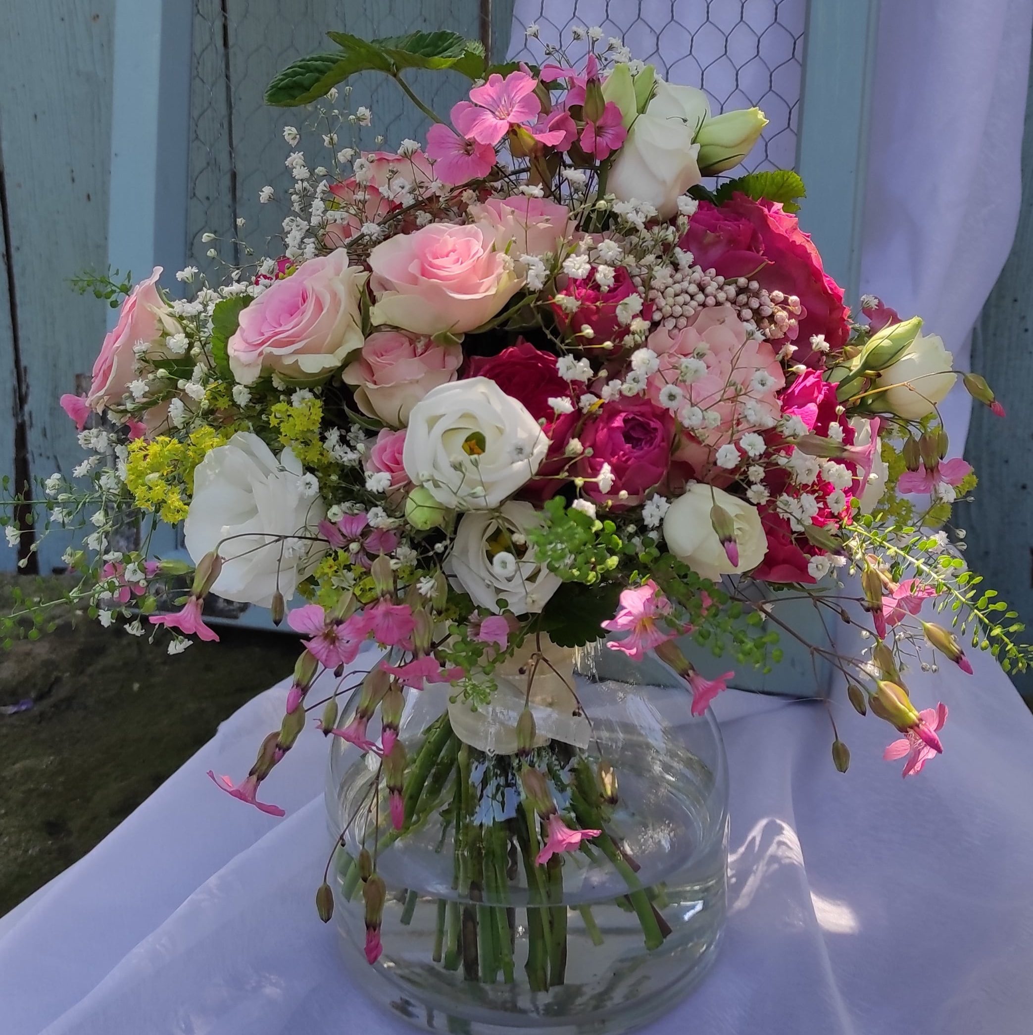 Bunter Sommerstrauß mit rosa und weißen Rosen in einer Glasvase vor rustikalem Hintergrund