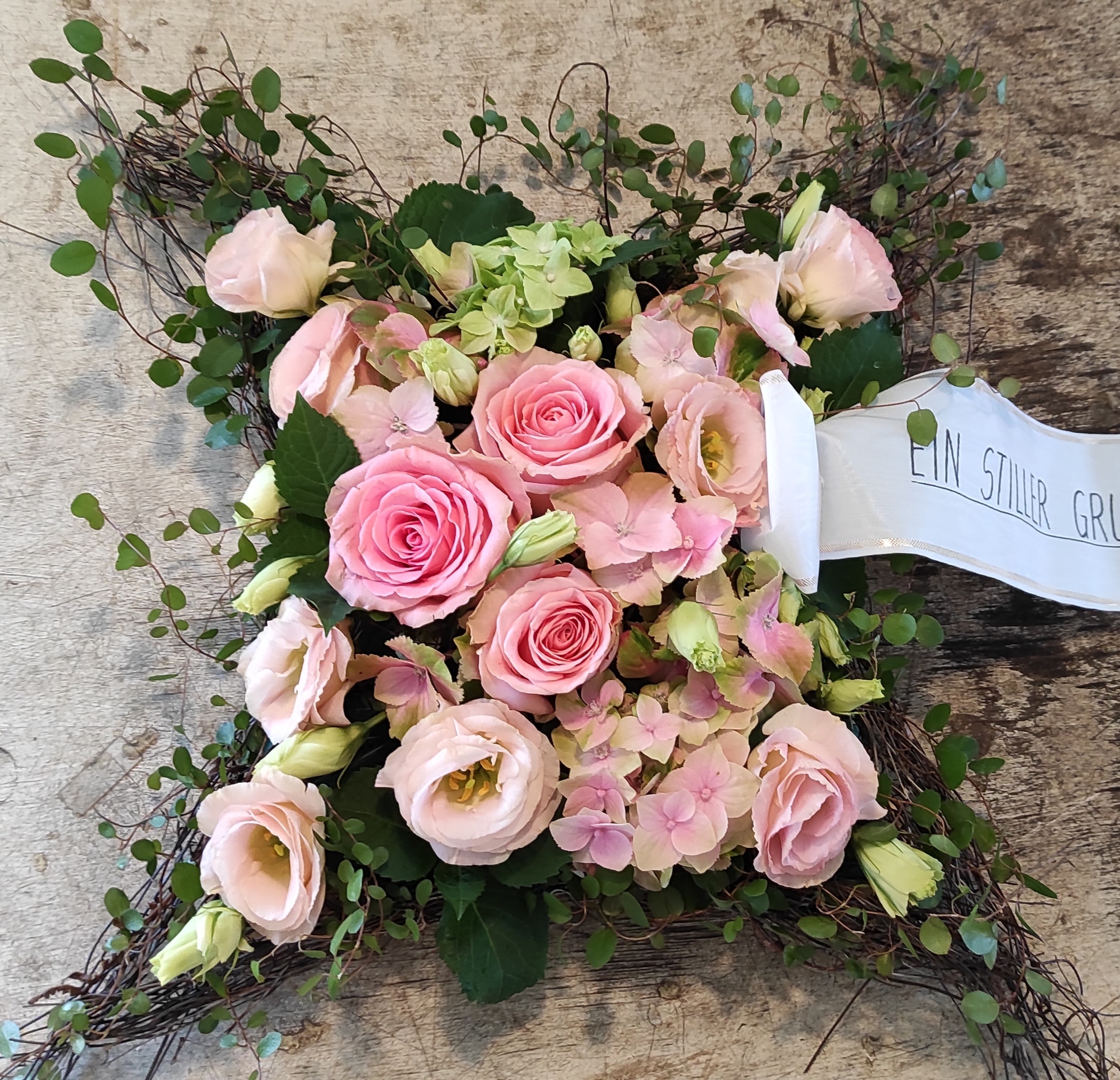 Quadratisches Trauerkissen aus rosa Rosen und Hortensien mit Rebenkranz und weißer Trauerschleife