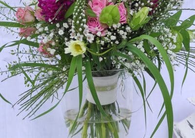 Sommerlich bunter Brautstrauß mit Wiesenblumen-Charakter, präsentiert in einer Glasvase