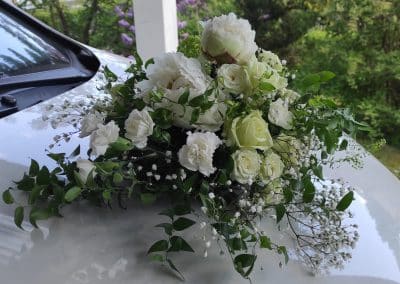 Hochzeitsfloristik Dresden Dittersbach: Weißer Autoschmuck mit Rosen und Nelken auf Motorhaube.
